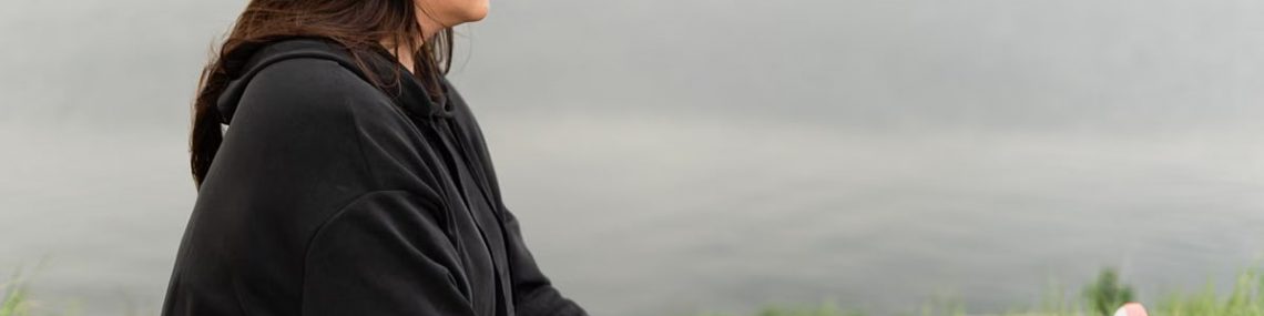 Woman meditating outdoors by a tranquil lakeside, fostering health and wellness.